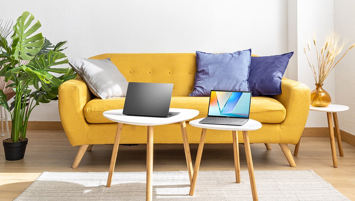 Twee Asus Vivobooks staan op witte driehoekige tafels in een grote en heldere woonkamer.