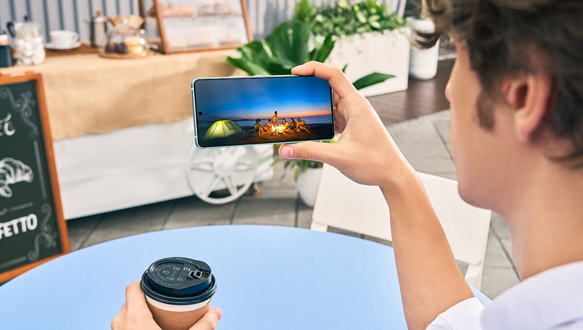 De hand van een man met een Ultra Asus Zenfone 12, terwijl hij naar het scherm kijkt dat een vreugdevuur op een strand vertegenwoordigt