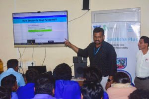 Een leraar, die voor een klaslokaal vol leerlingen staat, wijst naar een scherm waarop staat: "Hoe sterk is uw wachtwoord?" als onderdeel van een cyberveiligheidsles.