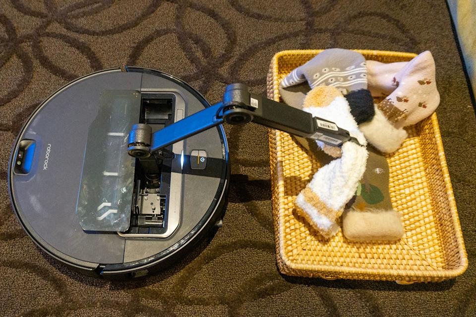 De Roborock Saros Z70 gebruikt zijn robotarm om een ​​handvol sokken in een bak te plaatsen. 