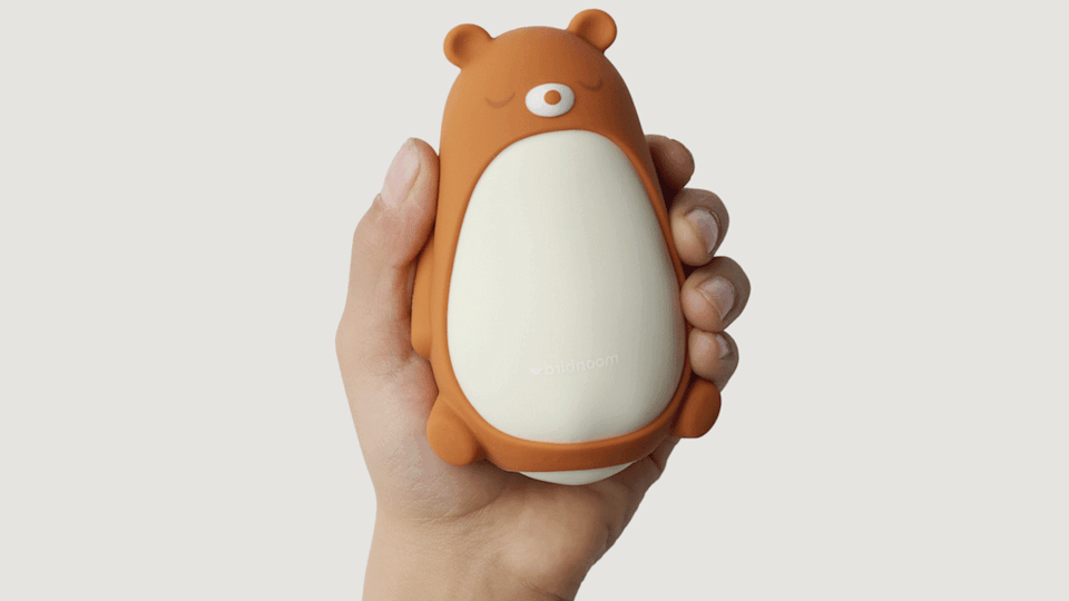 Eén hand houdt de Moonbird Moonbuddy vast. Het apparaat heeft een teddybeerbehuizing. 