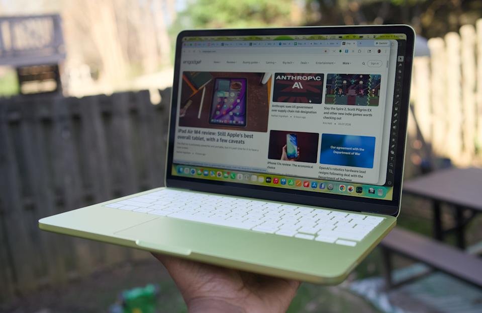 Een MacBook Neo in citruskleur vastgehouden met één hand.